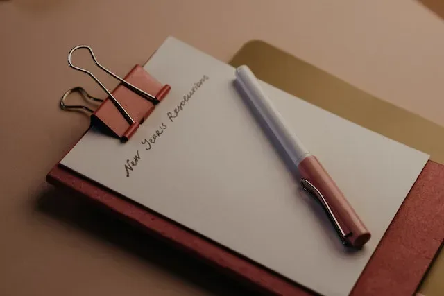 A notebook on the table and a pen on top with the words new year resolution scribbled on it.
