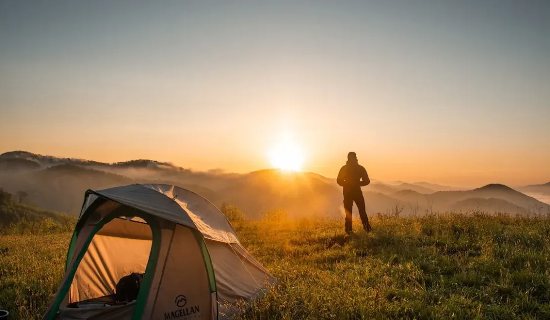 Sunrise: A man outside his tent looking towards the sun as it rises in the horizon